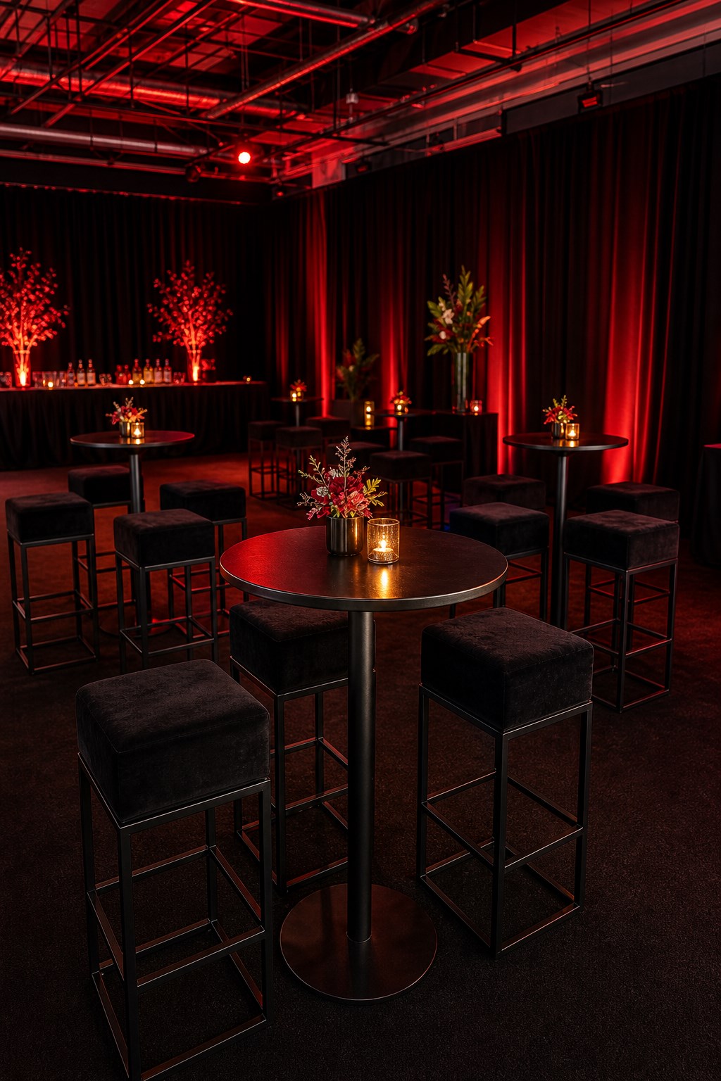 Black high cocktail tables with padded stools in a red lit evening reception setup