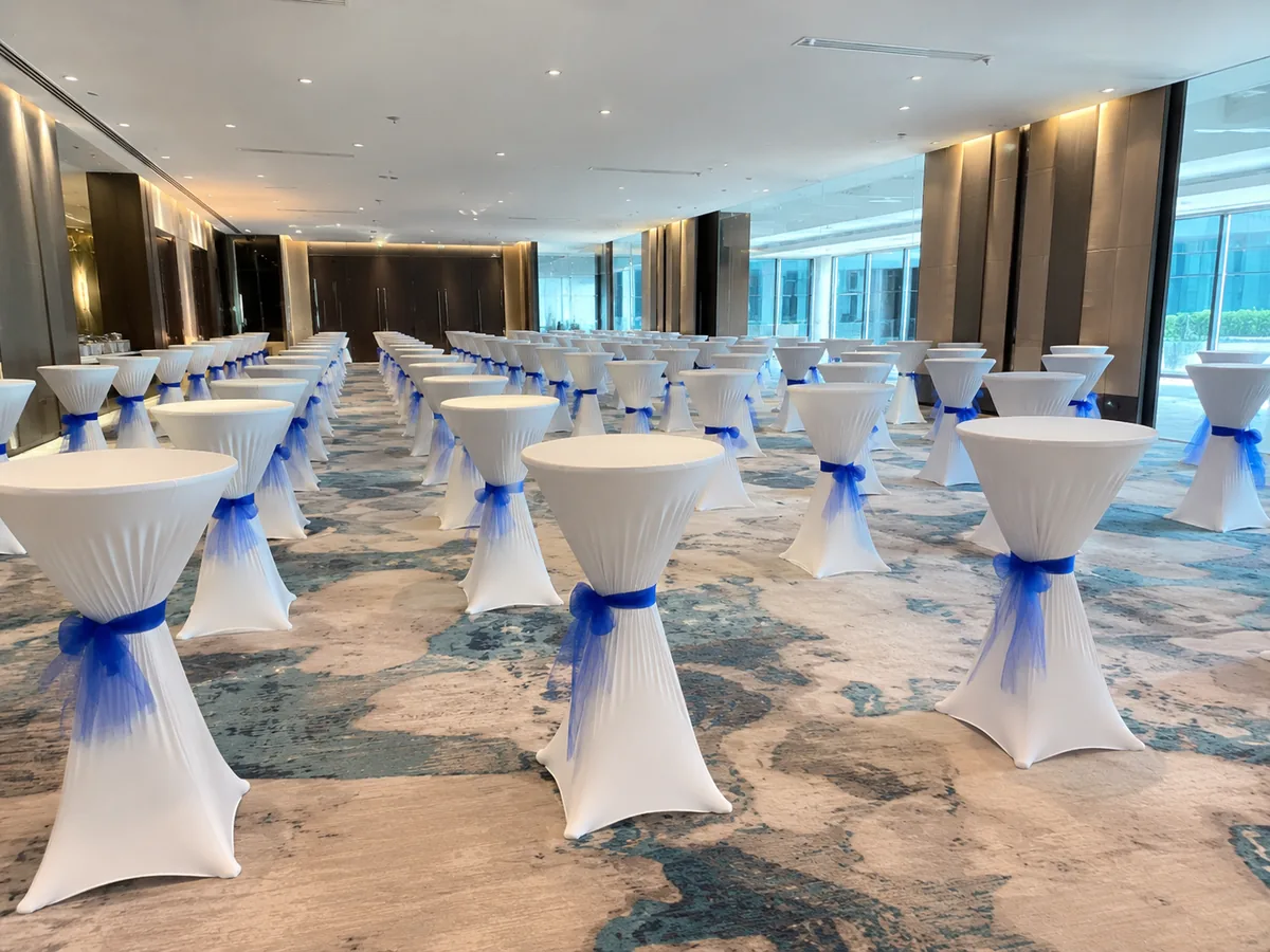White bar tables with blue sash arranged for an indoor event reception