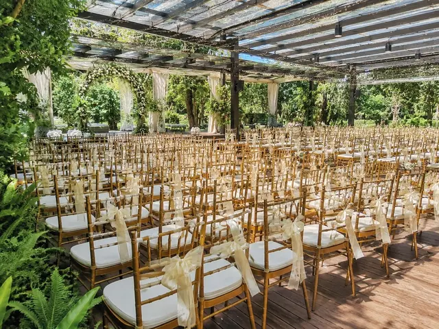 Gold Chiavari chairs in a covered garden wedding setup with white cushions and ribbon detail