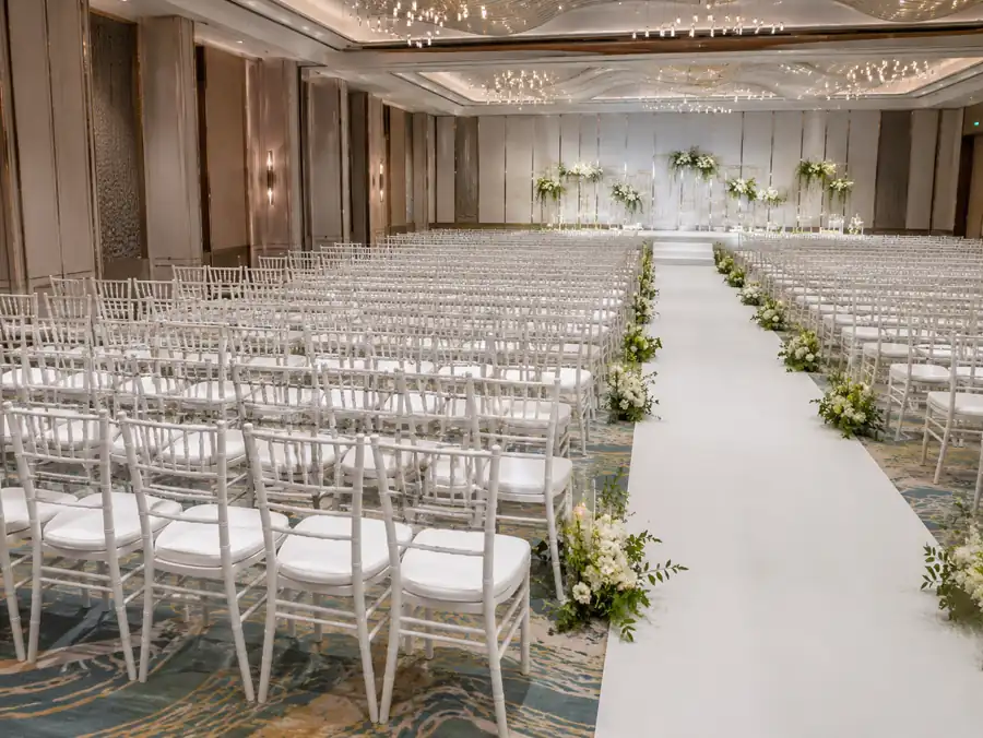 White Chiavari chairs beside a hotel ballroom wedding aisle with floral decor