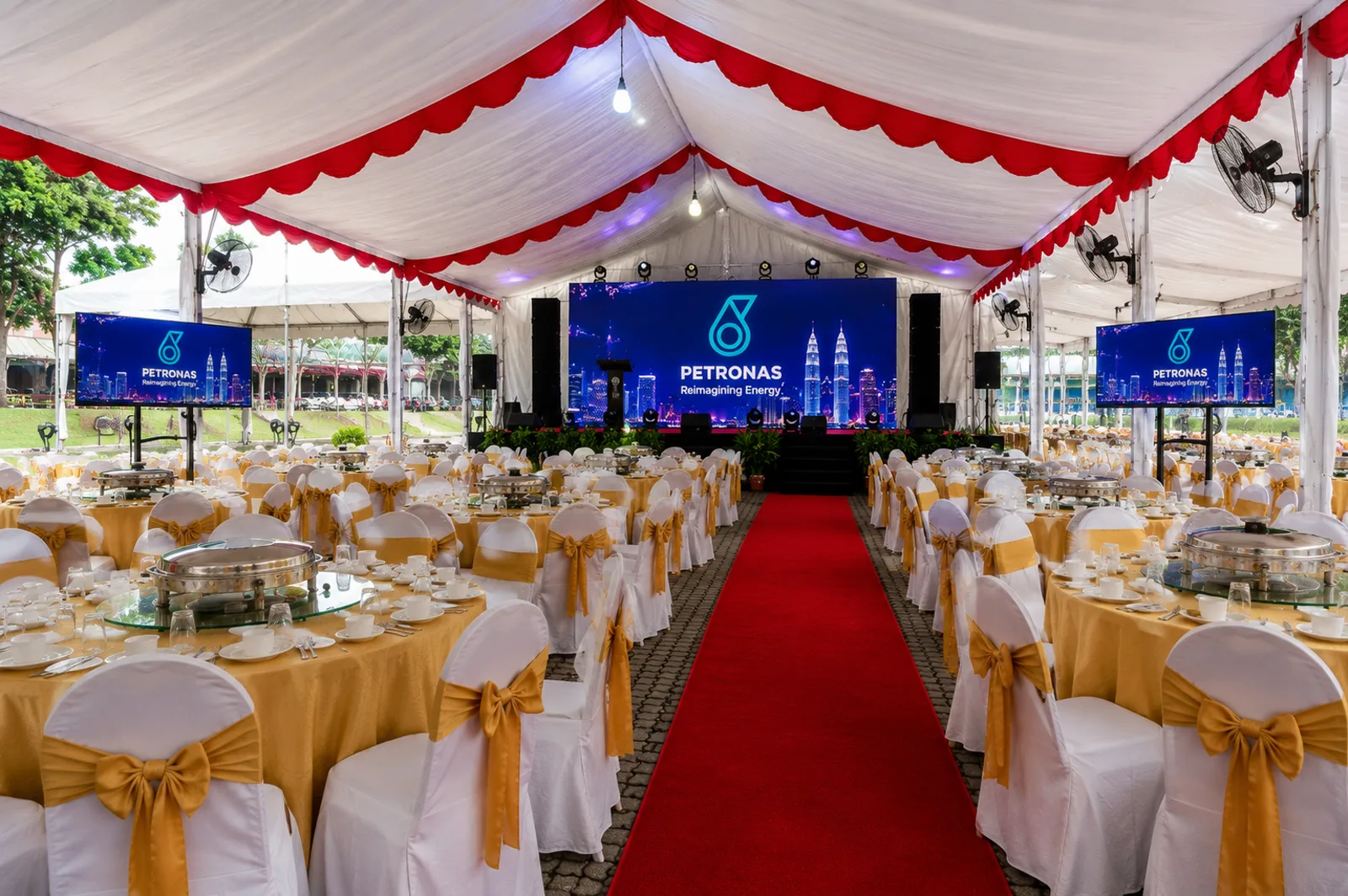 Corporate canopy dinner setup with red carpet, gold table covers and covered banquet chairs