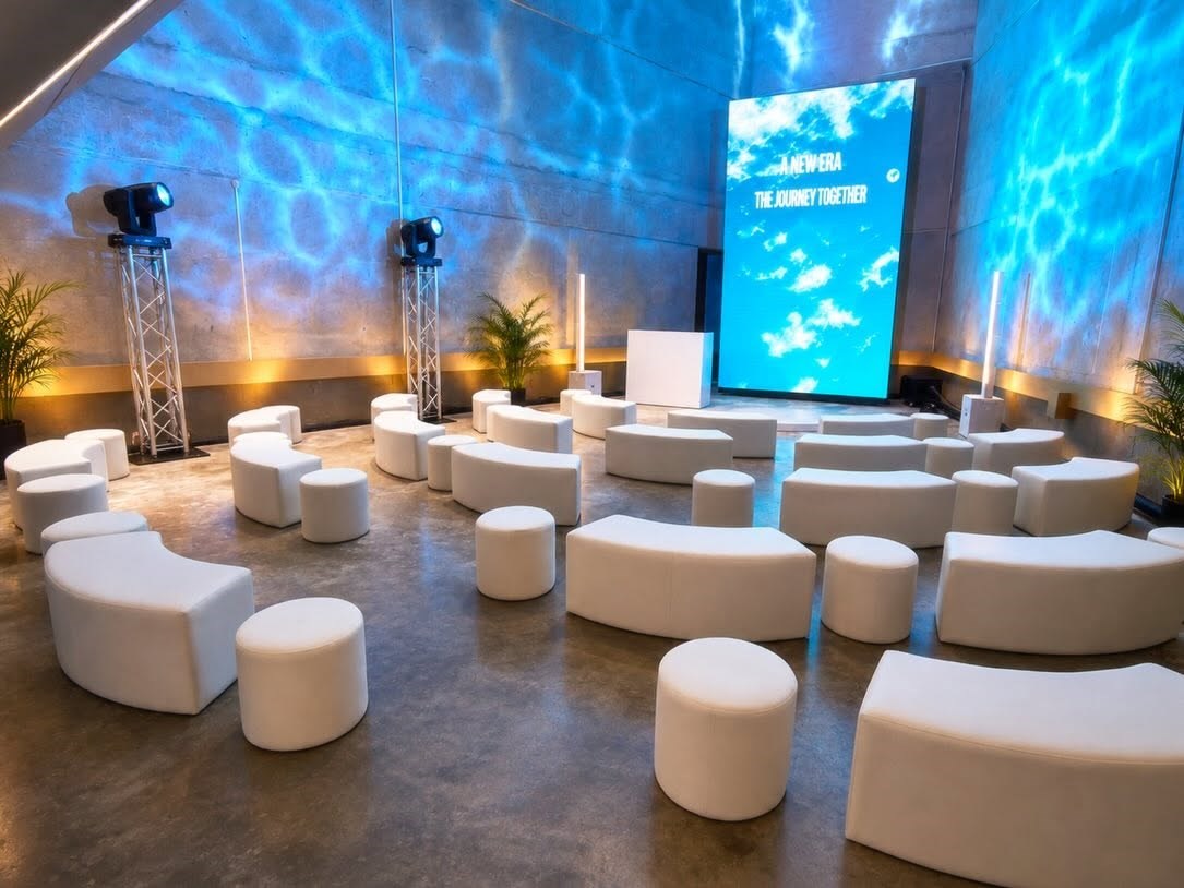 White curved lounge benches and round ottomans arranged with blue event lighting