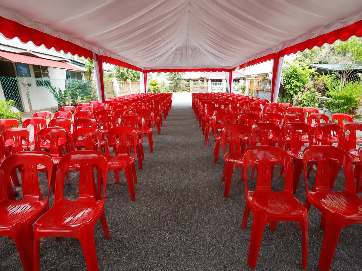 Red plastic chairs arranged in long rows under a canopy
