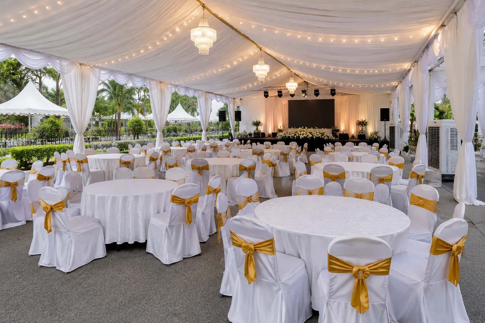 Large canopy dinner layout with round tables and covered chairs near stage