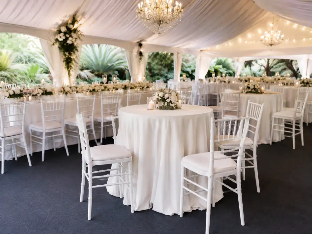 White Tiffany chairs with round tables under a wedding canopy