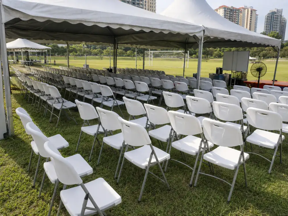 White folding chairs arranged under a canopy on a field for an outdoor event