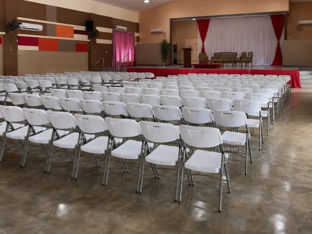 White folding chairs arranged in a hall facing a stage