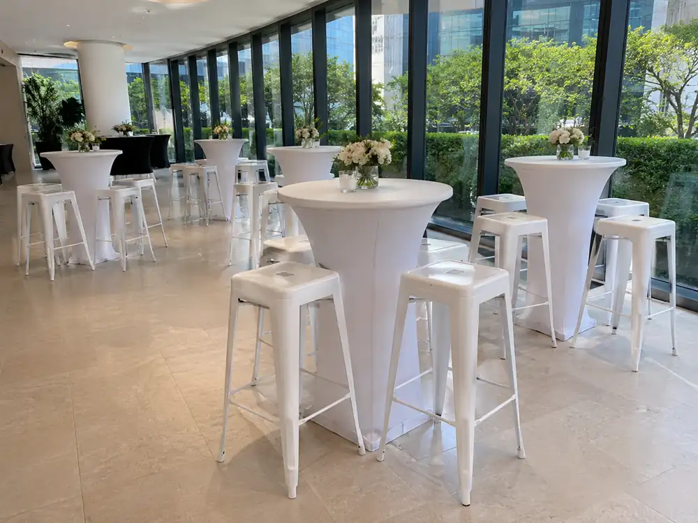 White Tolix bar stools with white cocktail tables near glass windows